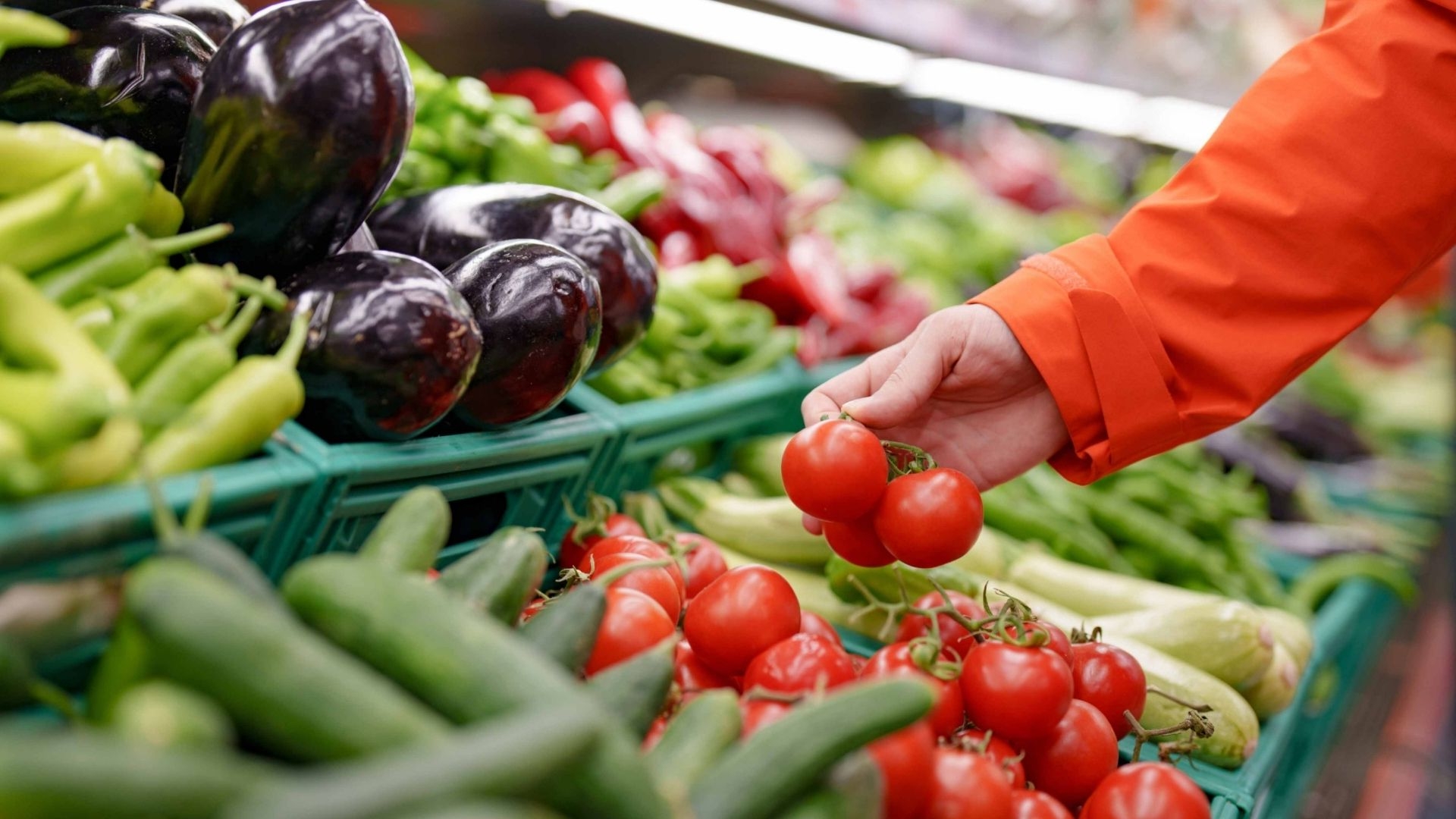 A person choosing a red tomatoes from the fresh produce section.