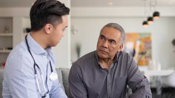A man discussing his health concerns with a doctor while seated on a couch.
