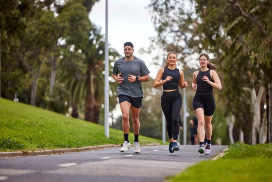Two women and a man run through a leafy park