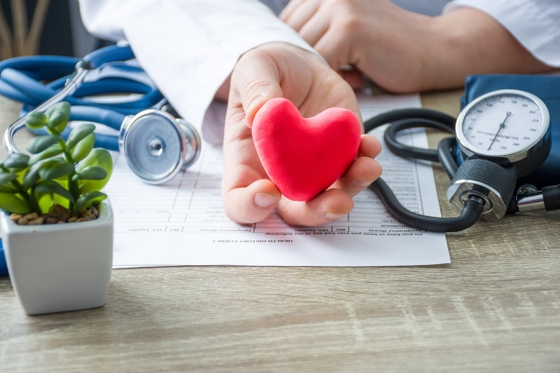 A doctor holding a red heart with a stethoscope, symbolizing care and medical expertise.
