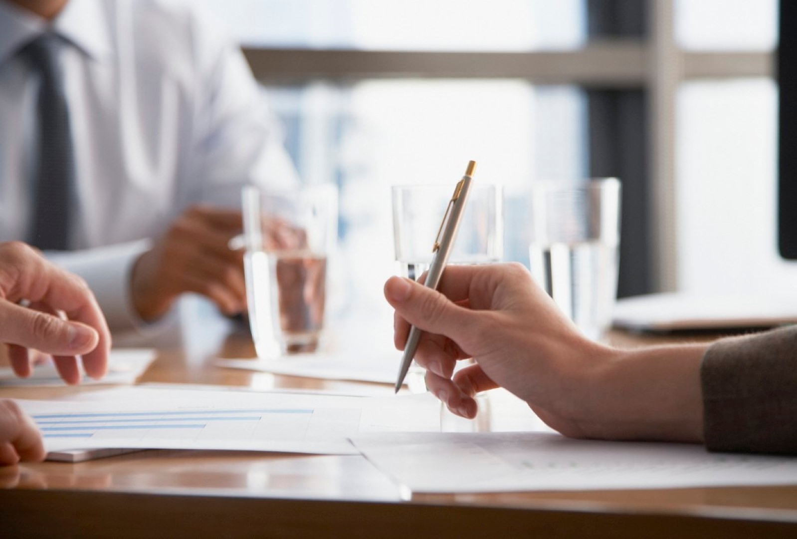 A woman's hand is shown holding a pen, she is at a table with others at a meeting