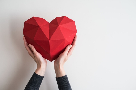 A woman holding a red paper heart on a white background, symbolizing love and affection. ❤️