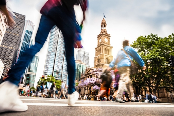A bustling cityscape with pedestrians strolling amidst towering buildings, accompanied by a majestic clock tower in the background.