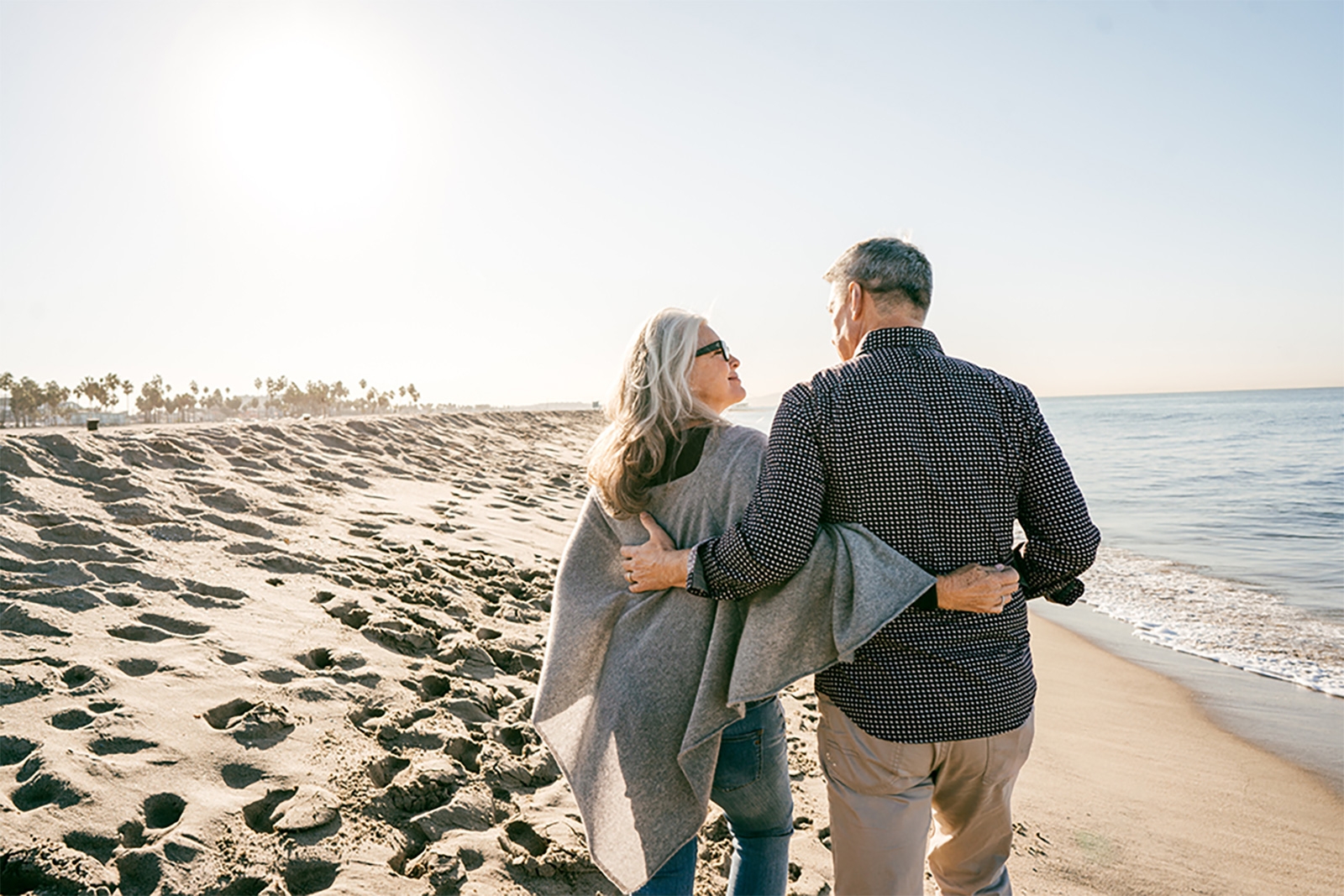 An elderly couple strolling along the sandy beach, enjoying a peaceful walk by the ocean's edge.