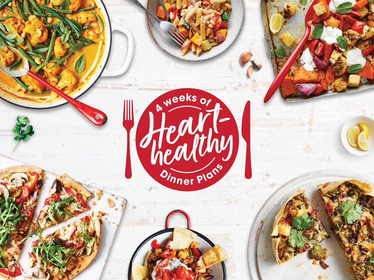 A variety of colorful and healthy dishes are arranged around a central red circle that reads '4 weeks of Heart-healthy Dinner Plans' with a red fork and knife on either side. The dishes include vegetable curry, a mixed vegetable stir-fry, roasted vegetables, two types of pizza with various toppings, and a dish with tortilla chips. There are also lemon wedges and garlic cloves scattered around the table.